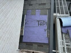 アスファルトシングル屋根の剥がれた部分に粘着性ルーフィングシートを貼っている作業。