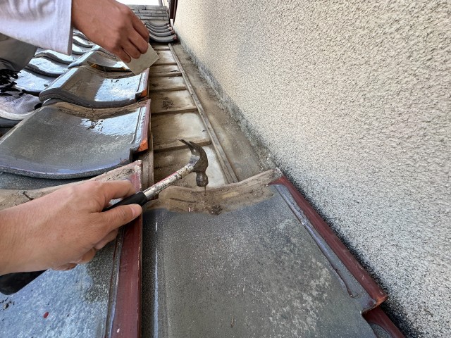 壁際の瓦を戻して釘で固定している作業